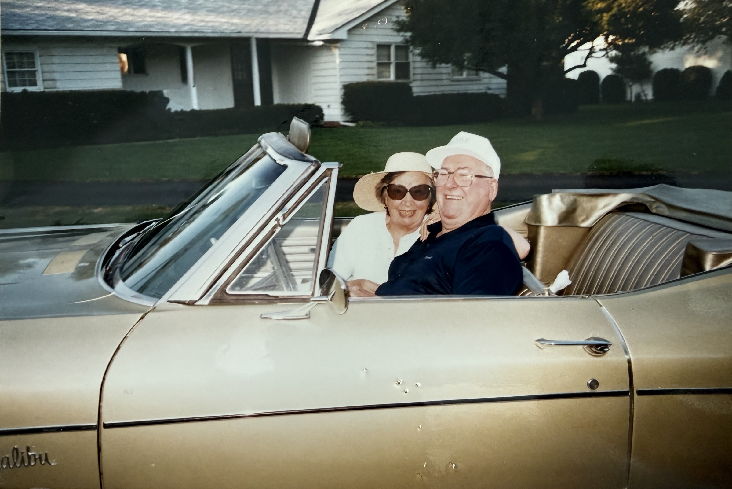 Gene and Betty smiling together in a gold convertible